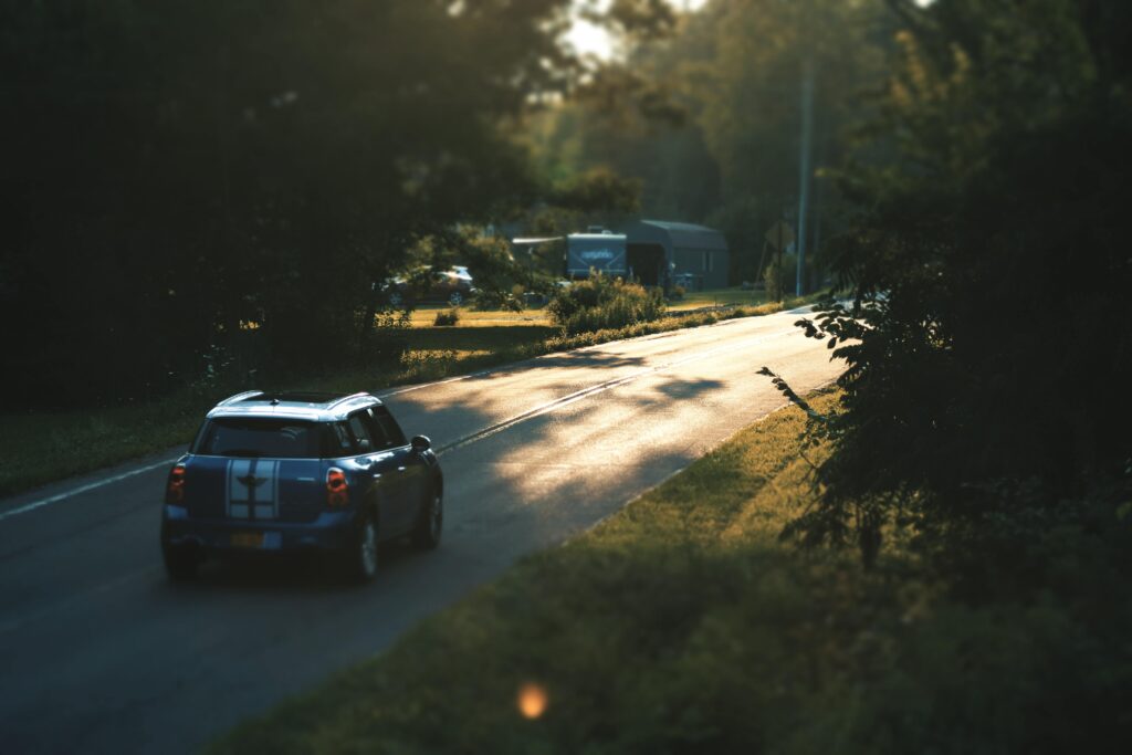 Замками Золочівщини A blue car travels down a quiet countryside road surrounded by lush greenery, bathed in daylight.